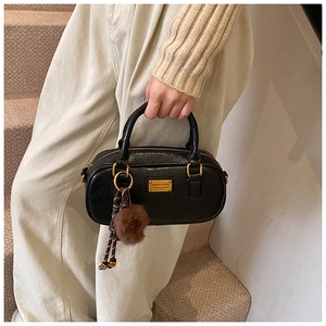 Close-up of black Boston pillow bag with golden logo plate and brown pom-pom charm