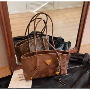 Détail d'un sac cabas en cuir verni marron avec logo métallique et pendentif cloche