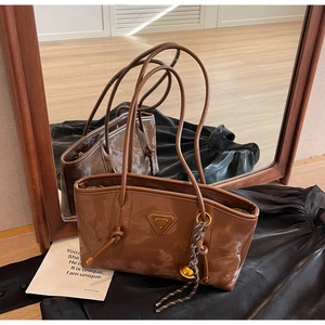 Détail d'un sac cabas en cuir verni marron avec pendentif doré et logo triangle