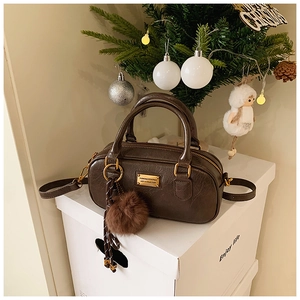 Close-up of deep coffee Boston bag with wrinkled texture, gold plate and plush charm