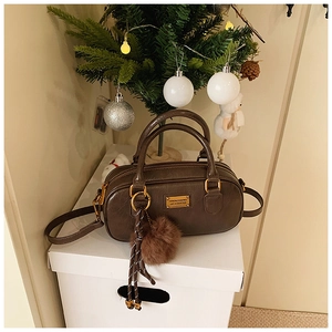 Detail of dark brown Boston bag with plush ball charm and gold hardware by a Xmas tree