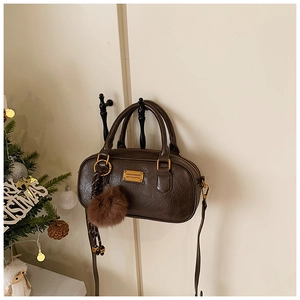 Close-up of a dark brown textured Boston bag with a fuzzy pom-pom and gold hardware
