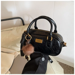 Detail of black oil wax leather handbag with golden logo plate and brown fur ball charm