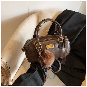 Detailed view of coffee brown boston bag featuring vintage leather texture and fuzzy ball charm