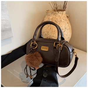 Close-up of vintage dark brown boston bag with golden logo plate and fuzzy pompom charm