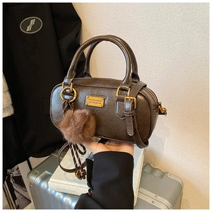 Close-up of brown Boston handbag with gold plaque, fur ball charm and leather texture