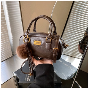 Detailed macro of dark brown textured Boston bag with gold logo and plush keychain