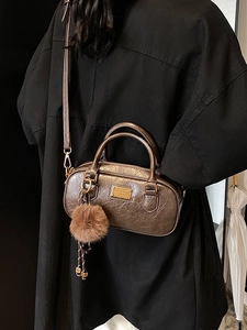 Metallic bronze Boston bag with plush ball charm and top handles in a classic retro style