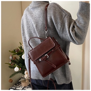 Details einer dunkelbraunen Retro-Ledertasche mit Silberschnalle auf grauem Pullover