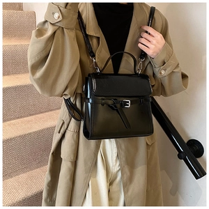 Detail einer eleganten schwarzen Lackleder-Handtasche kombiniert mit beigem Trenchcoat