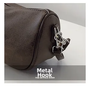 Close-up of silver hardware hooks and retro brown leather texture on a barrel bag
