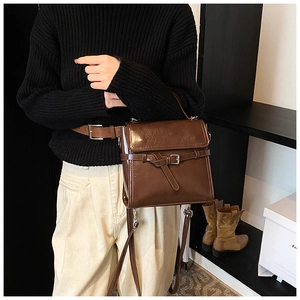 Detail einer dunkelbraunen, glänzenden Lederhandtasche, als Crossbody-Tasche getragen