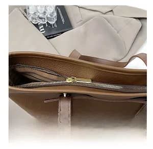 Detail of smooth gold zipper on brown lychee grain leather tote bag with striped lining