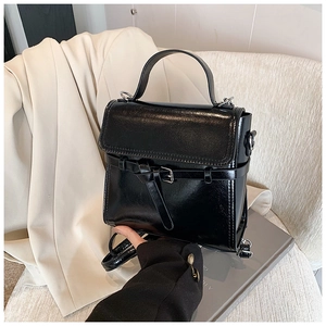 Detail einer glänzenden schwarzen Ledertasche mit Metallschnalle und festem Tragegriff