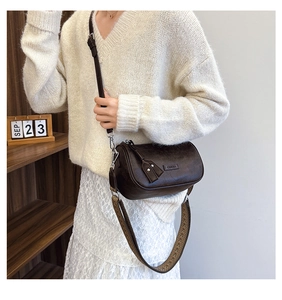 Brown vintage cylinder crossbody bag styled with a wide geometric woven shoulder strap