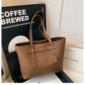 Detail of brown litchi pattern leather tote with gold hardware and fashion lettering