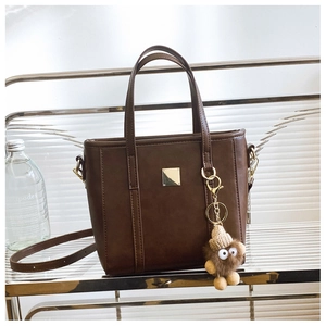 Dark brown leather tote bag detail with golden metal plate and plush bear charm