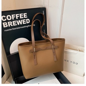 Detail of a brown lychee-grain leather tote bag featuring a gold buckle and luxury texture