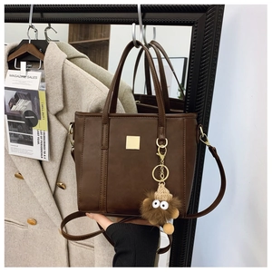 Detail shot of a dark brown matte leather tote bag with gold buckle and plush charm decoration
