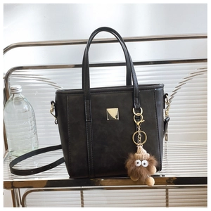 Detail of black faux leather tote with golden metal hardware and plush monster charm