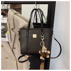 Detail of a dark brown crossbody tote with golden square buckle and cute monster plush charm