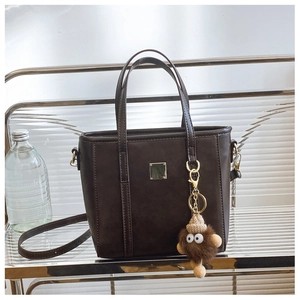 Detail view of dark brown PU leather handbag featuring a cute monster charm and square metal tab