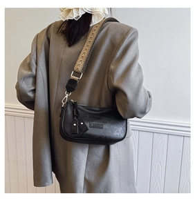 Detail of a black textured shoulder bag with a vintage woven wide strap on a model
