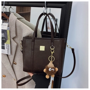 Detail of dark brown leather tote with gold hardware and plush charm by a mirror