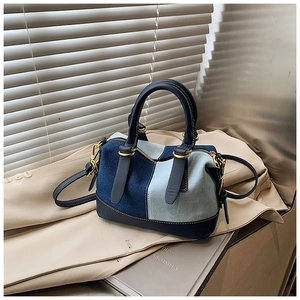 Dettaglio borsa Boston in denim bicolore con finiture dorate su un blazer beige