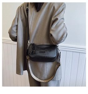 Detail of black leather crossbody bag with colorful woven strap on grey blazer