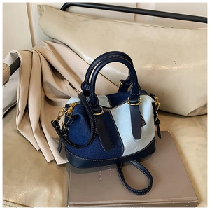 Dettaglio della borsa Boston in denim patchwork con manici in pelle blu e finiture dorate