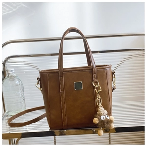 Detailed shot of brown leather bag with silver buckle and brown furry monster charm