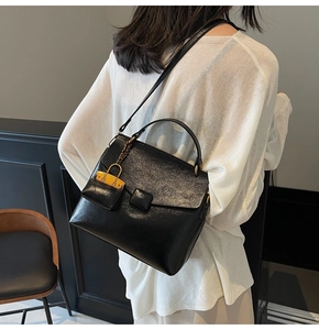 Detail of black leather shoulder bag with miniature orange charm and flap closure