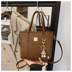 Detail view of brown vintage satchel with metal plate and plush monster keychain
