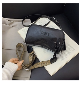 Detail of black textured crossbody bag with wide geometric strap on white magazine