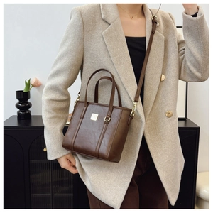 Detail of elegant dark brown leather tote bag with gold hardware and metal plate