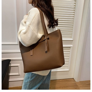 Detail of dark brown leather tote bag with pebble texture and decorative strap on shoulder