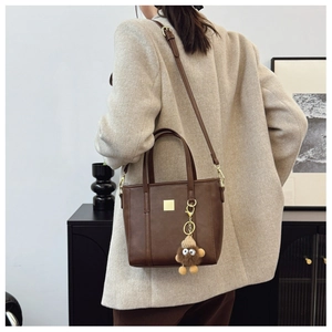 Detail of dark brown leather handbag with plush charm and adjustable strap on a model
