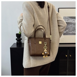Close-up of a dark brown crossbody bucket bag with gold hardware and a plush charm