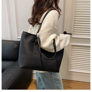 Close-up of black lychee grain leather tote bag with wide shoulder straps and vertical stitching