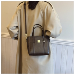 Chocolate brown faux leather bucket bag shown as a crossbody on a beige trench coat
