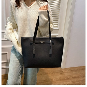 Close-up of a black leather tote bag with gold trim and textured finish on a model