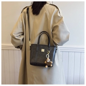 Detail of a black square bucket bag with a plush charm on a beige trench coat