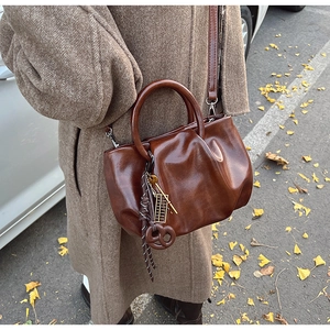 Détail du sac seau plissé vintage marron foncé avec charme d'abaque sur feuilles d'automne