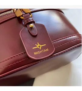 Close-up of the burgundy leather texture, gold zipper, and logo tag on the luxury box bag