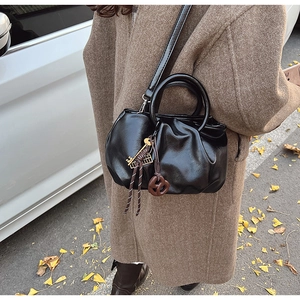 Détail du sac seau plissé noir avec breloques dorées porté sur un manteau en tweed