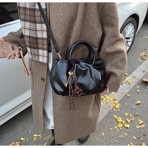 Détail d'un sac seau plissé noir avec poignée ronde et breloques dans un décor d'automne