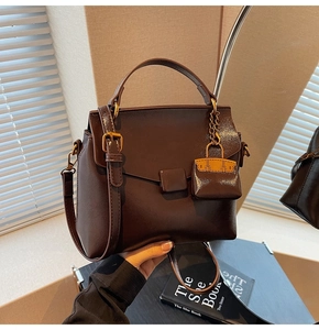 Detail of dark brown leather handbag with a miniature bag charm and adjustable strap