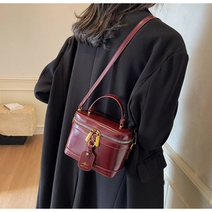 Detail of burgundy box bag with top handle and gold zipper worn over a black coat