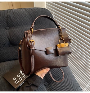 Detail of a dark brown faux leather trapezoid handbag with a mini bag charm pendant